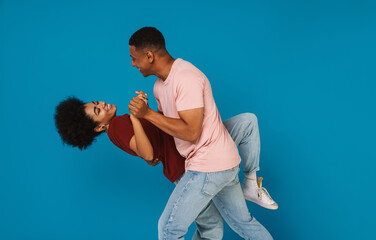 Excited positive afro couple dancing isolated over blue background