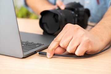 Close-up of a man's hand plugging a usb cable into a laptop from a camera at home