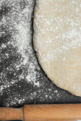raw bread dough with a rolling pin and flour scattered on a black table with space for text