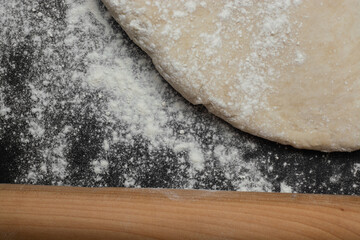 raw bread dough with a rolling pin and flour scattered on a black table with space for text