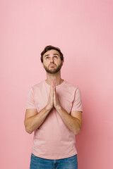 Bearded man making pray gesture while posing isolated over pink background