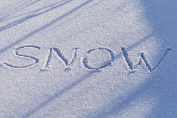 The inscription snow on a flat snowy surface with shadows from trees on a winter evening