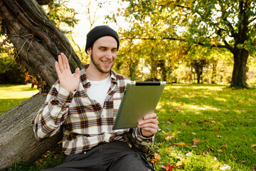 Cheerful man making video call via tablet and waving while sitting in park