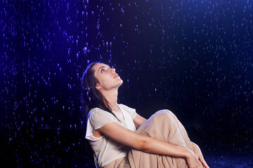 Beautiful young woman in a wet dress in the rain, shooting in the studio on a black background.