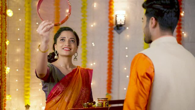 shoulder shot, Wife looking husband face through sieve during karva Chauth festival ceremony - concept of Indian custom, tradition and celebration