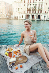 Lovely young woman picturesque picnic on the wooden gondola dock with rose wine, fruits and snack on wooden pier © blackday