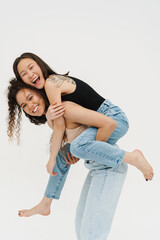 Cheerful girls doing piggyback ride isolated over white background