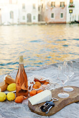 Fototapeta na wymiar Rose wine, fruits and snacks on the wooden pier during picturesque picnic on the wooden dock