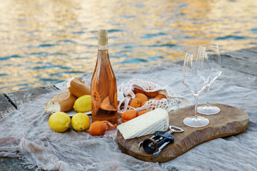 Rose wine, fruits and snacks on the wooden pier during picturesque picnic on the wooden dock