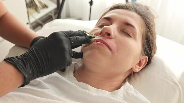 Waxing specialist on a woman removing hair on her facial mustache using sugar paste. Concept: beauty self-care depilation. Woman enjoy the process of hair removal from underarms, soft and smooth skin