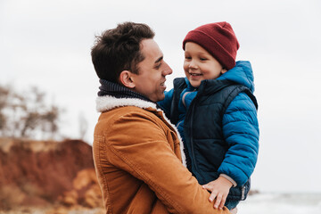 Fototapeta premium Smiling father holding son in his arms while spending fun time together on beach