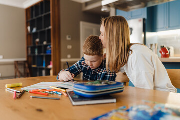 Mother kissing her son while sitting at table together in kitchen