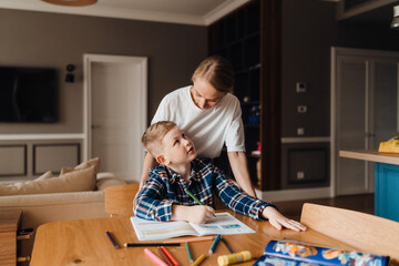 Beautiful mother helping her son with homework in kitchen
