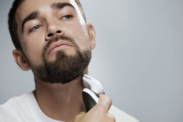 Young handsome man is using electric trimmer for beard shaving