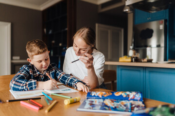 Beautiful mother helping her son with homework in kitchen