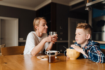 Young woman and her son having breakfast and eating corn flakes while sitting in kitchen