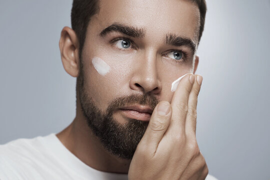 Young man is applying moisturizing cream on his face