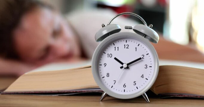 Tired woman sleeps on table with alarm clock and book
