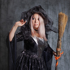 Cute witch with a broom, preparing to fly to the sabbath. Charming blonde in a long dress with a...