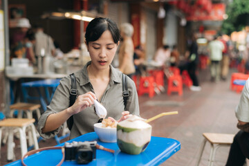 Happy young Asian woman backpack traveler enjoying street food at China town street food market in Bangkok, Thailand. Traveler checking out side streets.