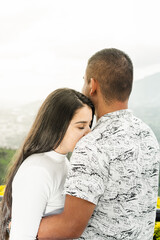 young woman leaning her face on her boyfriend's shoulder, while he looks at the landscape.