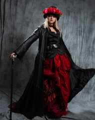 gorgeous Gothic lady in a long leather coat and a hat with roses, uses a cane.