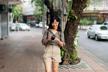 Fototapeta premium Young Asian woman backpack traveler using digital compact camera, enjoying street cultural local place and smile. Traveler checking out side streets. 