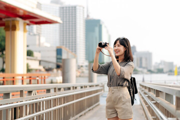Young Asian woman backpack traveler using a camera in express boat pier on Chao Phraya River in Bangkok. Journey trip lifestyle, world travel explorer or Asia summer tourism concept