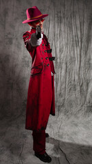 A stylish guy in a vampire costume, a red hat, a coat and tinted glasses. aiming a gun