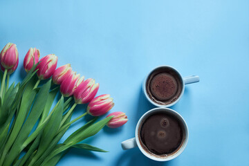 Bouquet of pink tulips on blue background. Two cups of hot, morning coffee in the shape of the number 8. Copy space. Mothers day