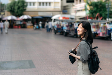 Young Asian woman backpack traveler using digital compact camera, enjoying street cultural local place and smile. Traveler checking out side streets. 