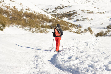 man walking through the snowy mountains with snowshoes on his back
