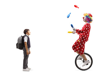 Full length shot of a schoolboy looking at a clown juggling and riding a unicycle