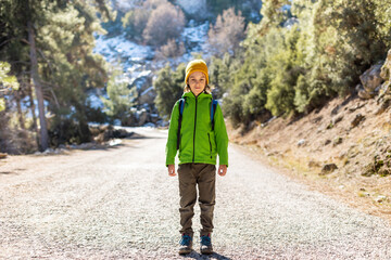 Fototapeta premium A boy with a backpack in the middle of a forest road, a child is exploring wildlife, a child is standing alone among the trees. Travel and hiking.