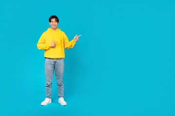 Positive Asian Teen Boy Pointing Fingers Aside Over Blue Background