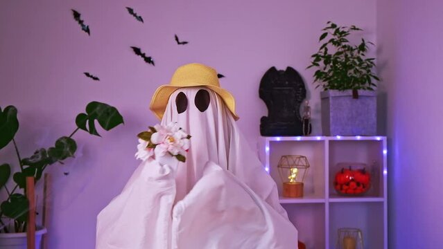 A ghost gardener in a straw hat sniffs flowers. Halloween concept. Funny ghost. Day of the Dead. Carnival costume.
