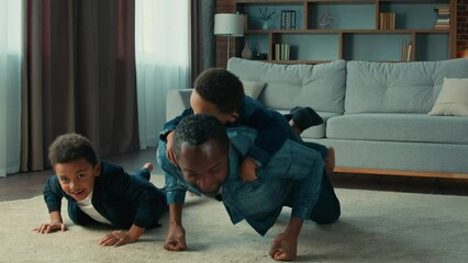 African American strong father with two children boys doing push ups on floor in living room family fitness at home. Sporty dad with son piggy back having fun exercise funny sport with child kids sons