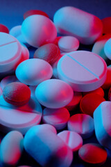 Extasy and drug concept. Close up shot of white and colored pills of different kind lit with red and blue neon lights.