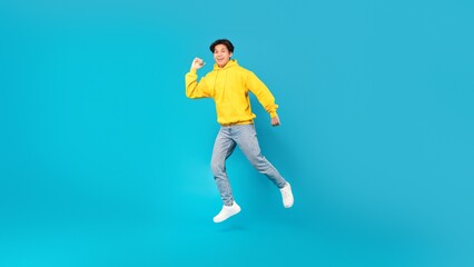 Joyful Chinese Teen Boy Jumping Smiling Posing Over Blue Background