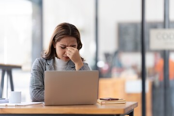 Fototapeta premium Young businesswoman working on laptop stressed has a headache and thinks hard from work at the office