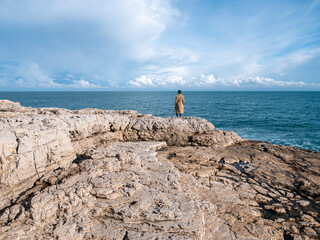 Woman isolated on the rocks looking at the sea in winter season