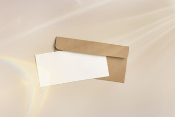 Blank paper card mock up and craft envelope on beige background with sunbeams. White empty festive...