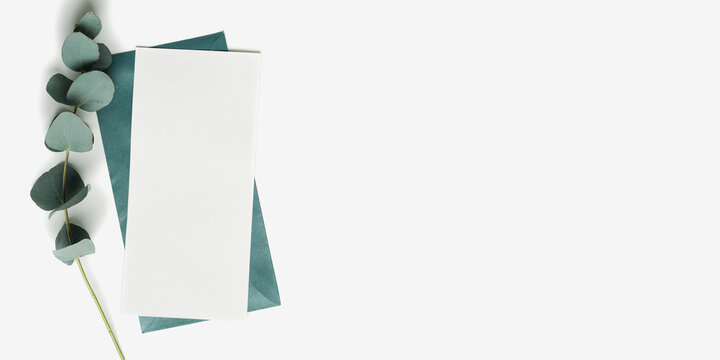 Teal color envelope and blank paper card mock up and branches eucalyptus leaves on white background. empty invitation on table. Minimal modern lifestyle photo. Flat lay, top view, copyspace
