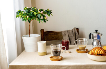 Fototapeta na wymiar Spring cozy breakfast concept. Two mugs with coffee and milk, croissants, plant with flowers, creamer, coffee pot, jam