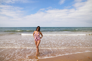 Beautiful and young latin woman is walking along the shore of the beach and posing for photos. Beautiful woman is on holiday on a paradise beach. Holiday and travel concept.