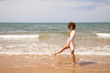 Young beautiful woman in bikini walking along the beach shore. The woman is enjoying her trip to a paradise beach while making different gestures and expressions. Holidays and travels.