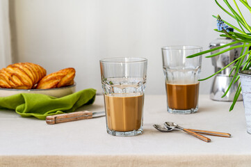 Spring cozy breakfast concept. Two glasses with coffee and milk, croissants, spring flowers, coffee pot, green napkin
