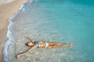 Sexy suntan perfect skin bikini woman relaxing on beach, lying in shallow water in turquoise mediterranean sea in Oludeniz Beach in Aegean Sea