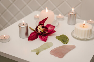 Spa center. Details decor in spa salon. Gua sha tool. Сandles, and orchid flowers on table. Facial massage for lifting, face therapy. Skincare concept. Cosmetology, body massage, spa procedure.
