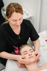 Obraz na płótnie Canvas Facial treatment, skincare concept. Relaxing massage. Cosmetologist making rejuvenating face procedures client in spa salon. Aesthetic cosmetology, face care. Girl getting face, head massage treatment